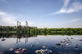 PAISAJE CONTAMINADO Se observa un lago con muchas bolsas de basura y en una de sus orillas varias chimeneas de fabrica.